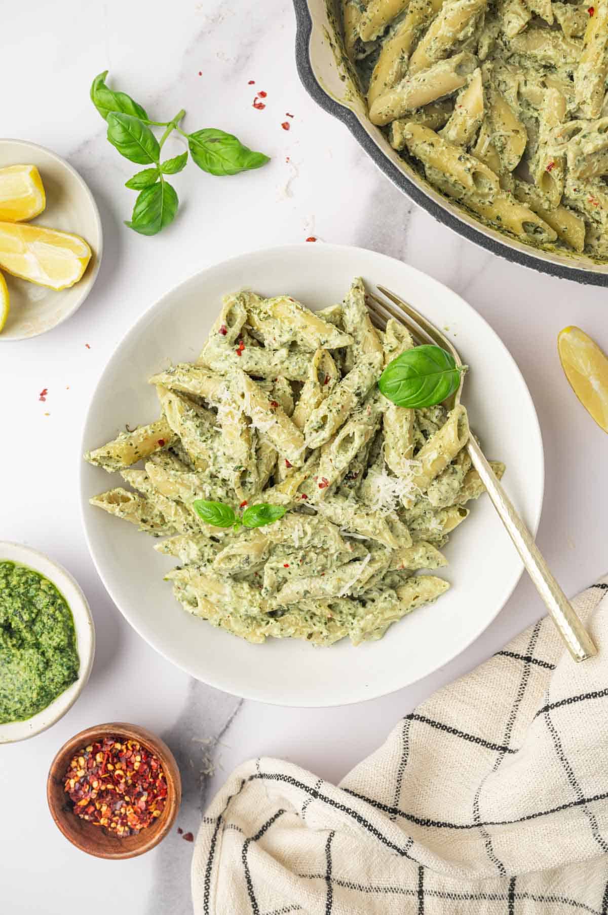 Pesto and ricotta pasta in a white bowl and a skillet