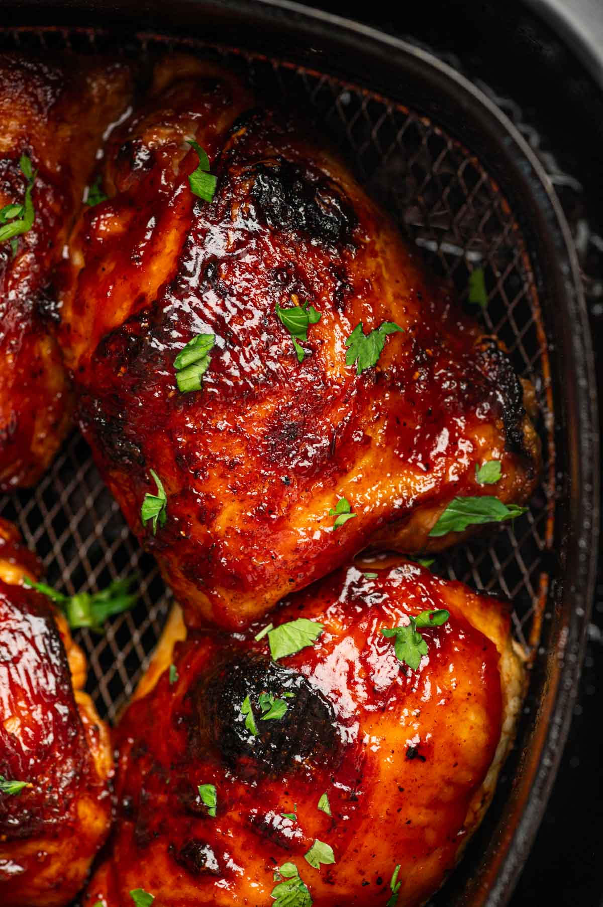 Bone-in, skin-on BBQ chicken thighs cooked to perfection in the air fryer, garnished with fresh parsley.