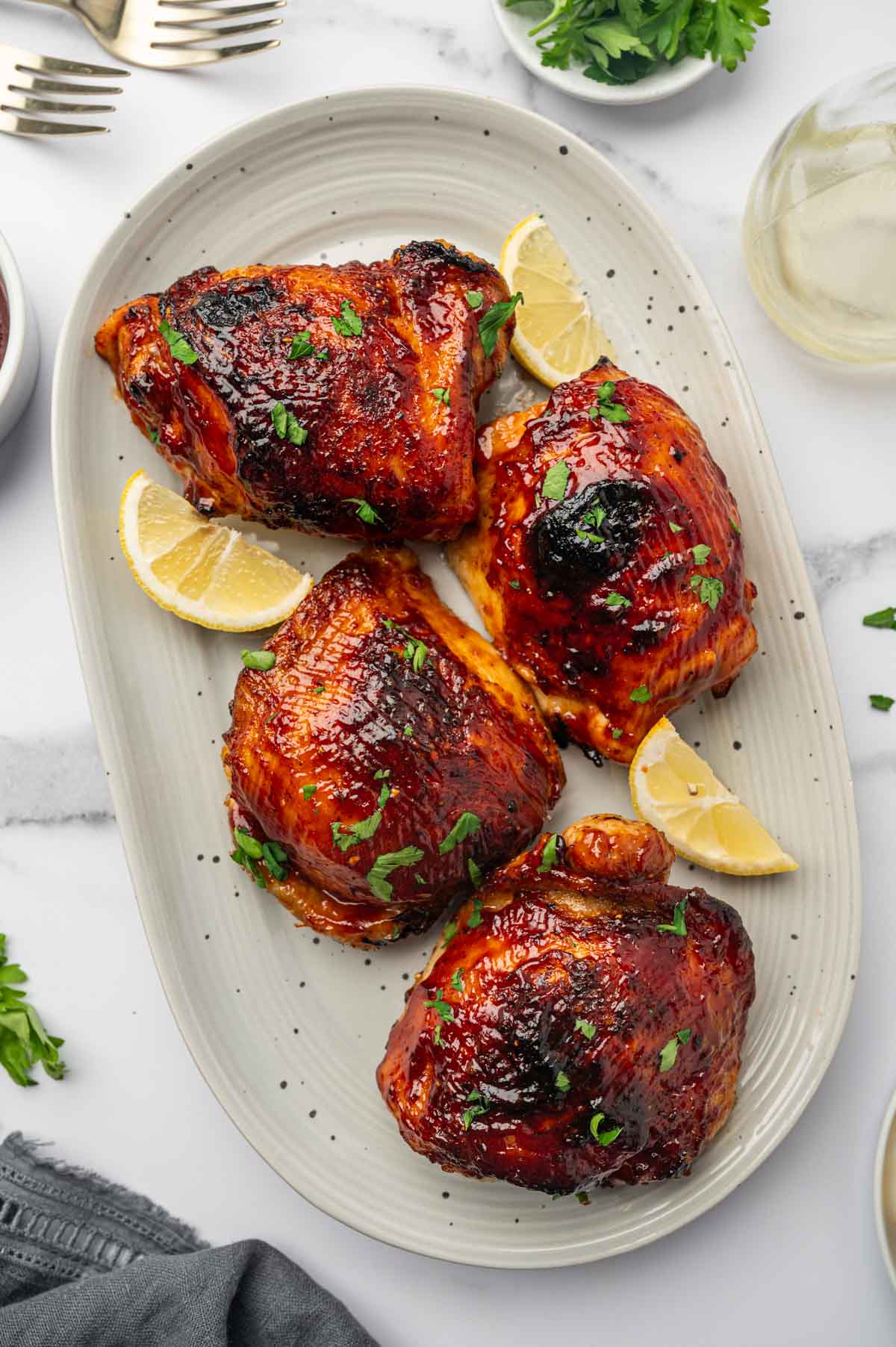 Golden brown air fryer BBQ chicken thighs with a rich, sticky glaze, served alongside a side extra sauce.