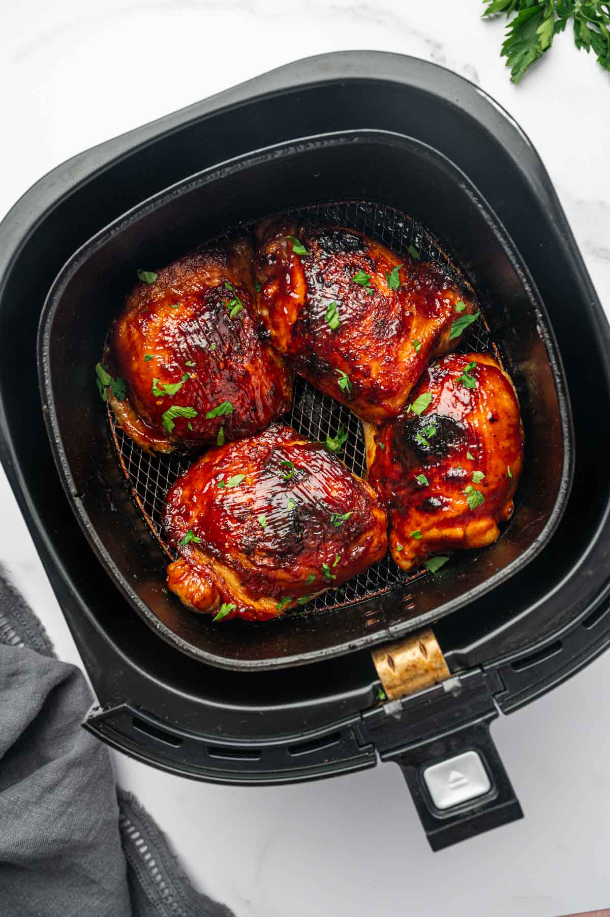 Golden brown air fryer BBQ chicken thighs with a rich, sticky glaze, in the air fryer basket.