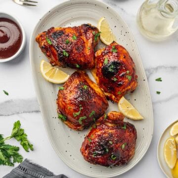 Juicy and crispy air fryer BBQ chicken thighs coated with a caramelized smoky barbecue glaze on a serving plate.