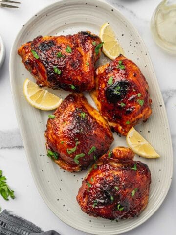 Juicy and crispy air fryer BBQ chicken thighs coated with a caramelized smoky barbecue glaze on a serving plate.