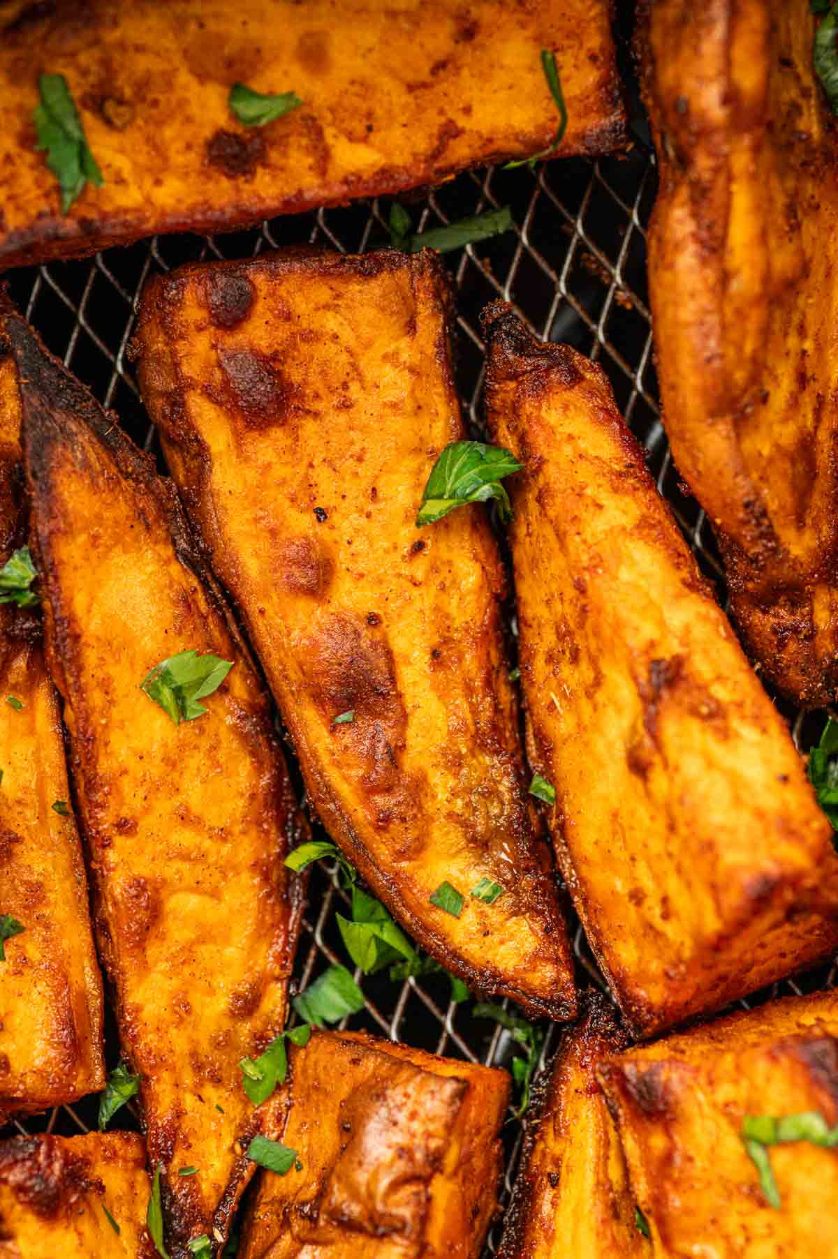 Close-up of crispy sweet potato wedges in an air fryer basket.