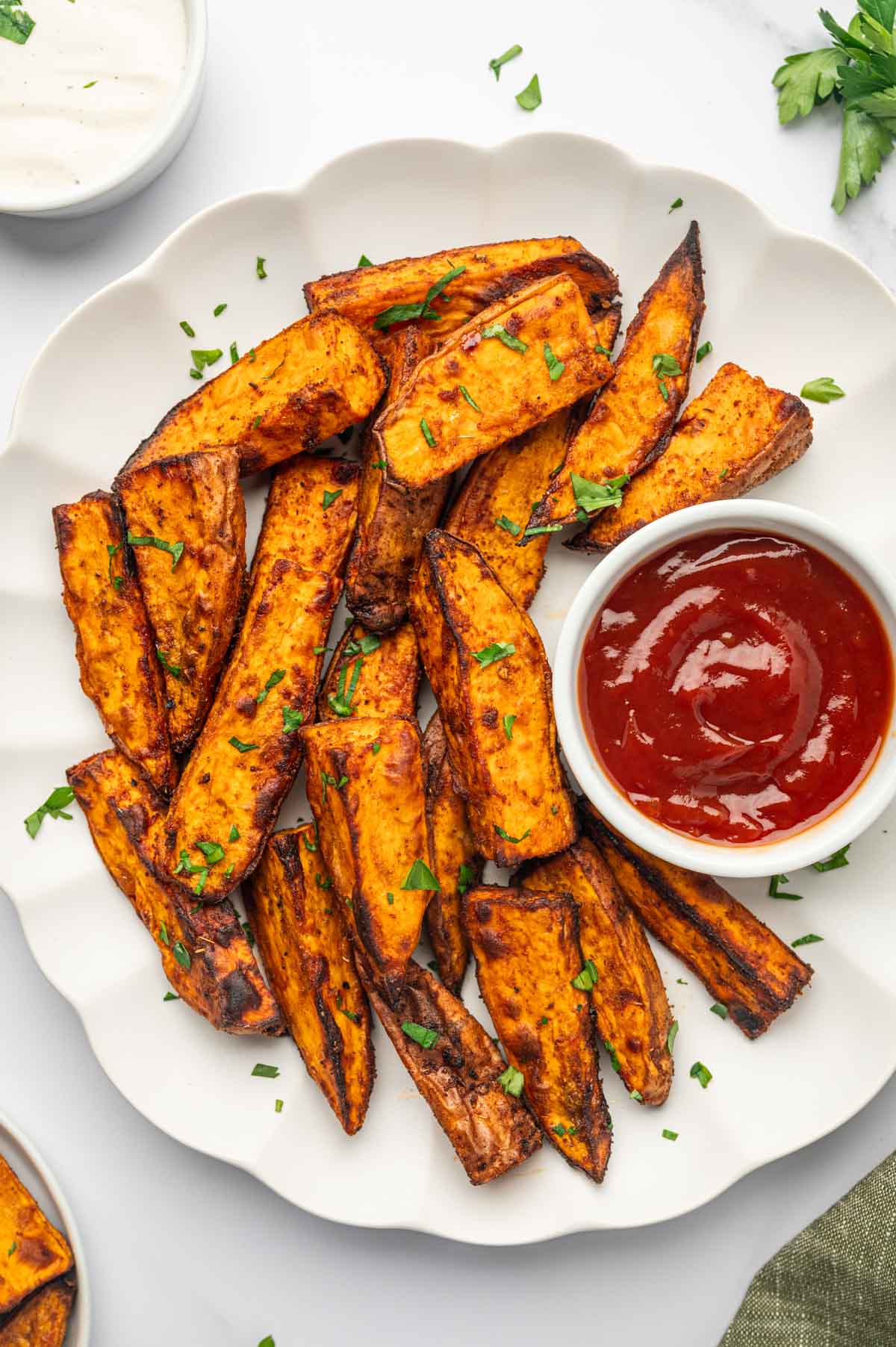 Crispy air fryer sweet potato wedges served with ketchup in a white plate.