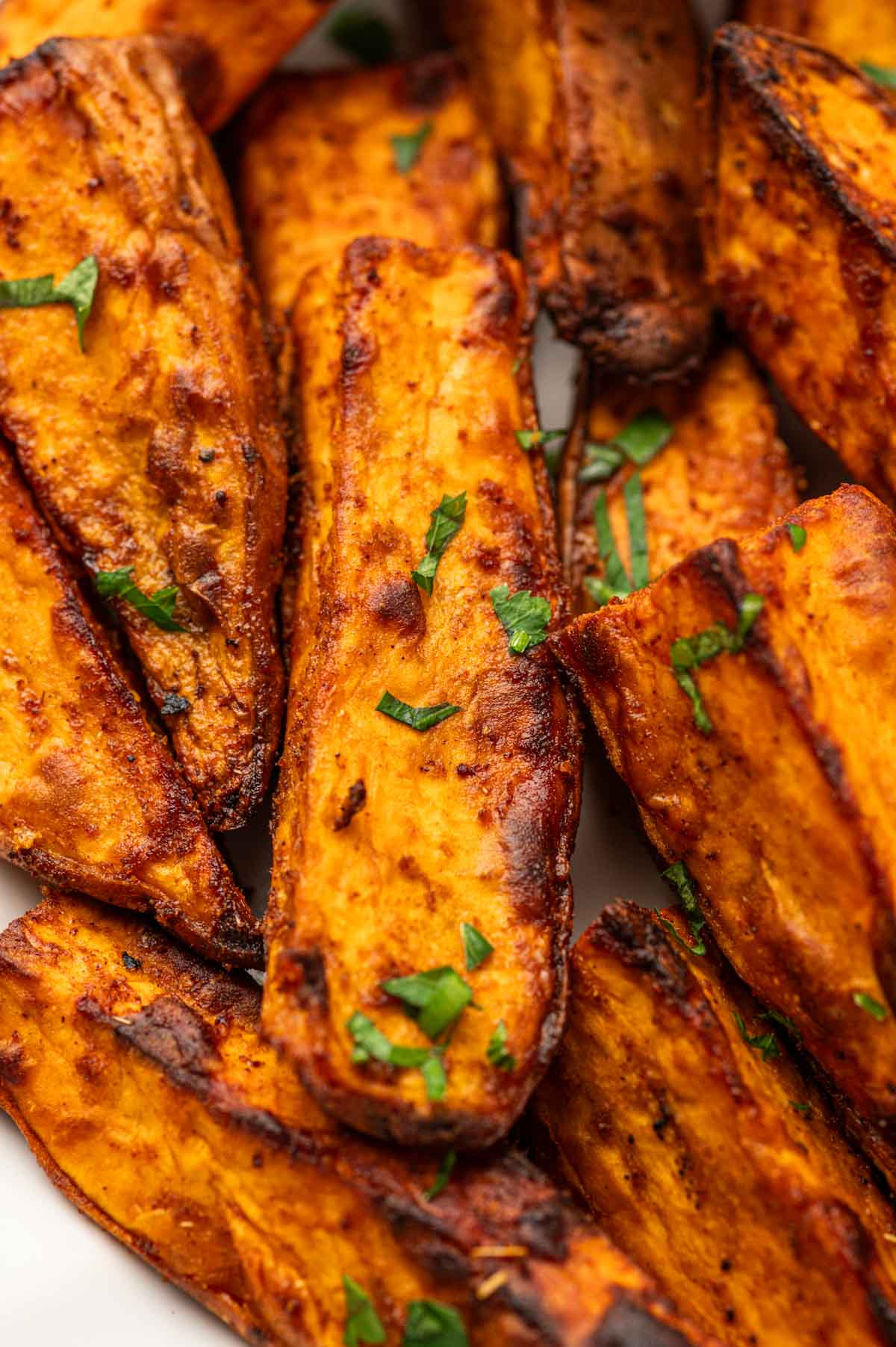 Close-up of crispy sweet potato wedges with fresh parsley garnish, perfect for snacks or side dishes.