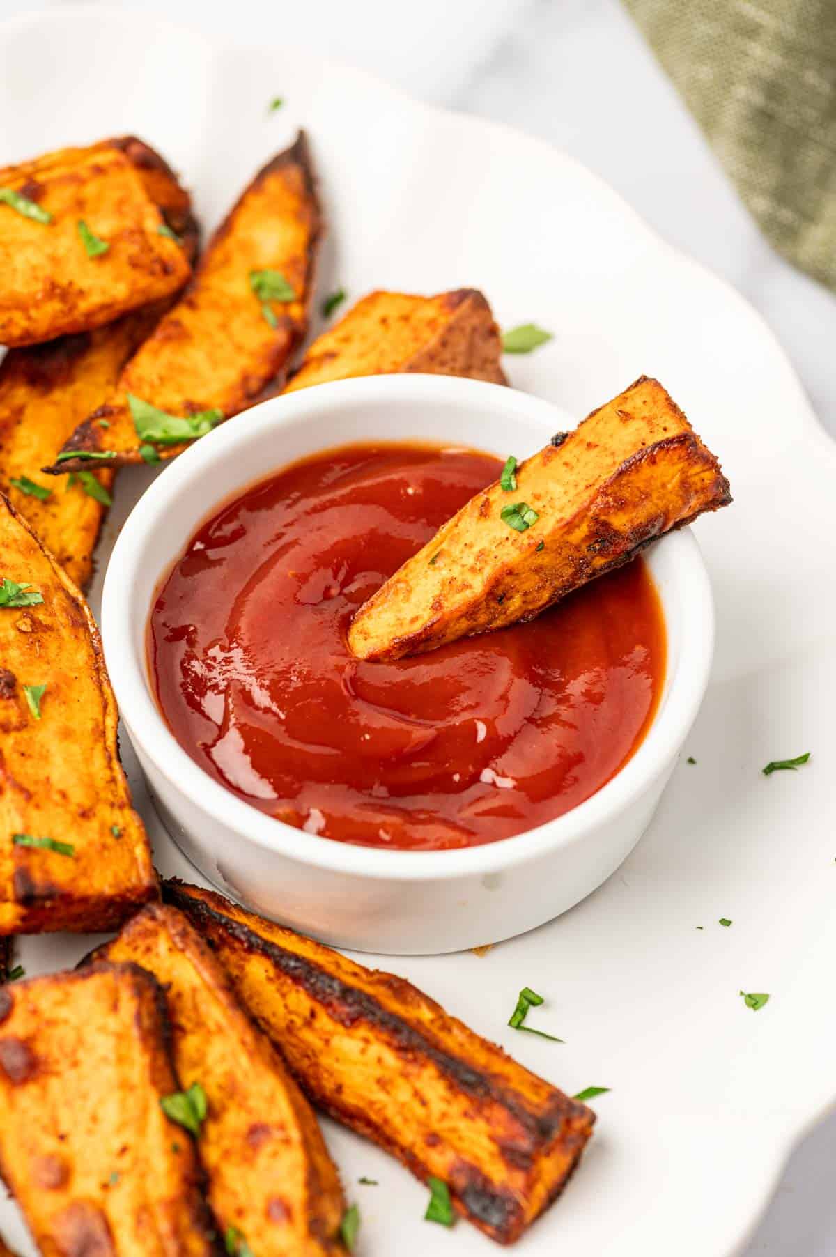 Healthy air fryer sweet potato wedges arranged on a plate with a side of ketchup and a fry dipped in.