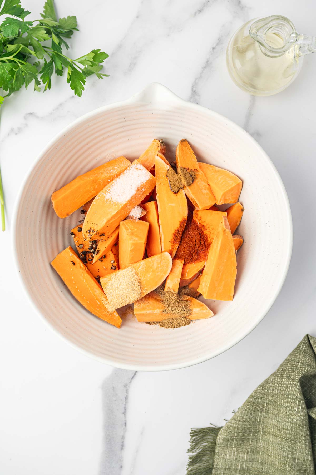 Adding the seasonings to the bowl of cut sweet potatoes .