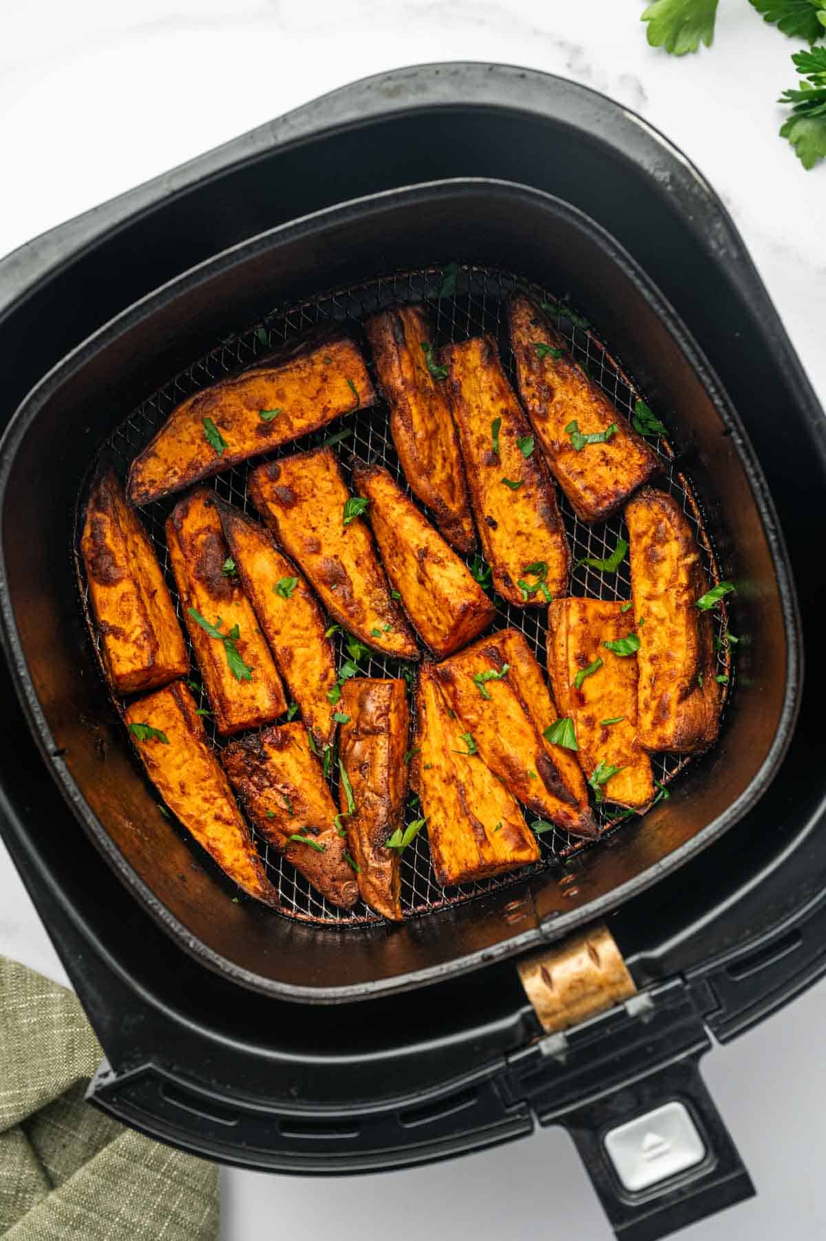 Close-up of crispy sweet potato wedges in an air fryer basket.