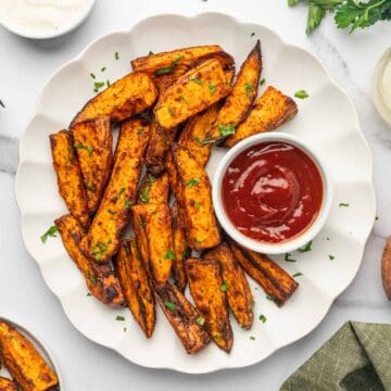 Crispy air fryer sweet potato wedges served with ketchup in a white plate.