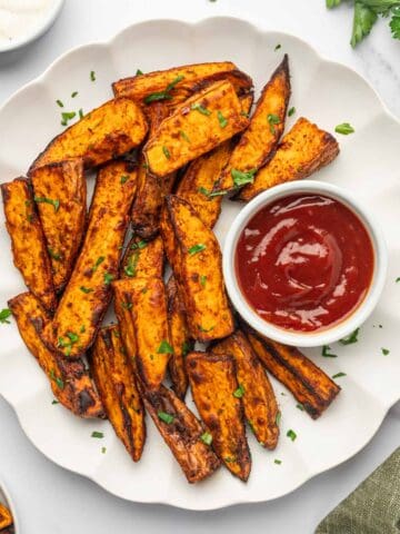 Crispy air fryer sweet potato wedges served with ketchup in a white plate.