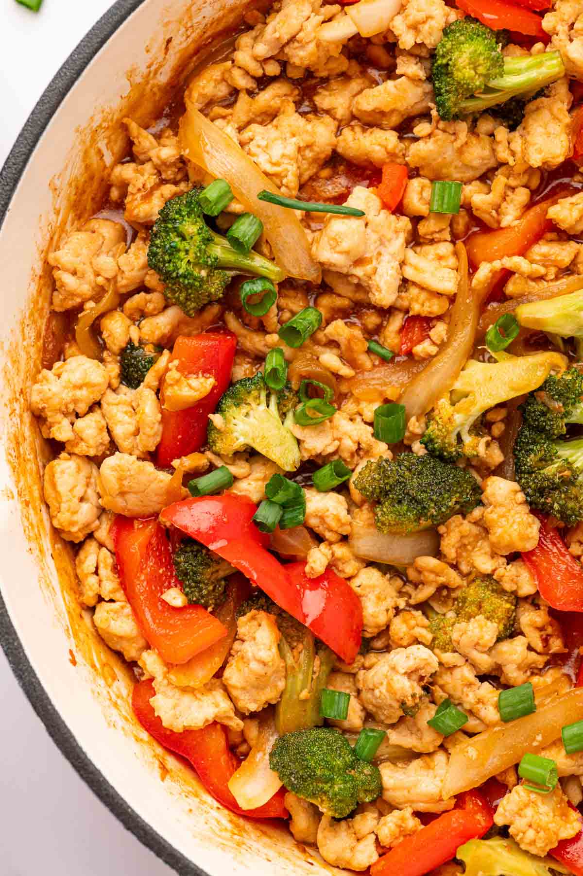 Quick and easy chicken stir stry with ground chicken and veggies in a white skillet close up shot.