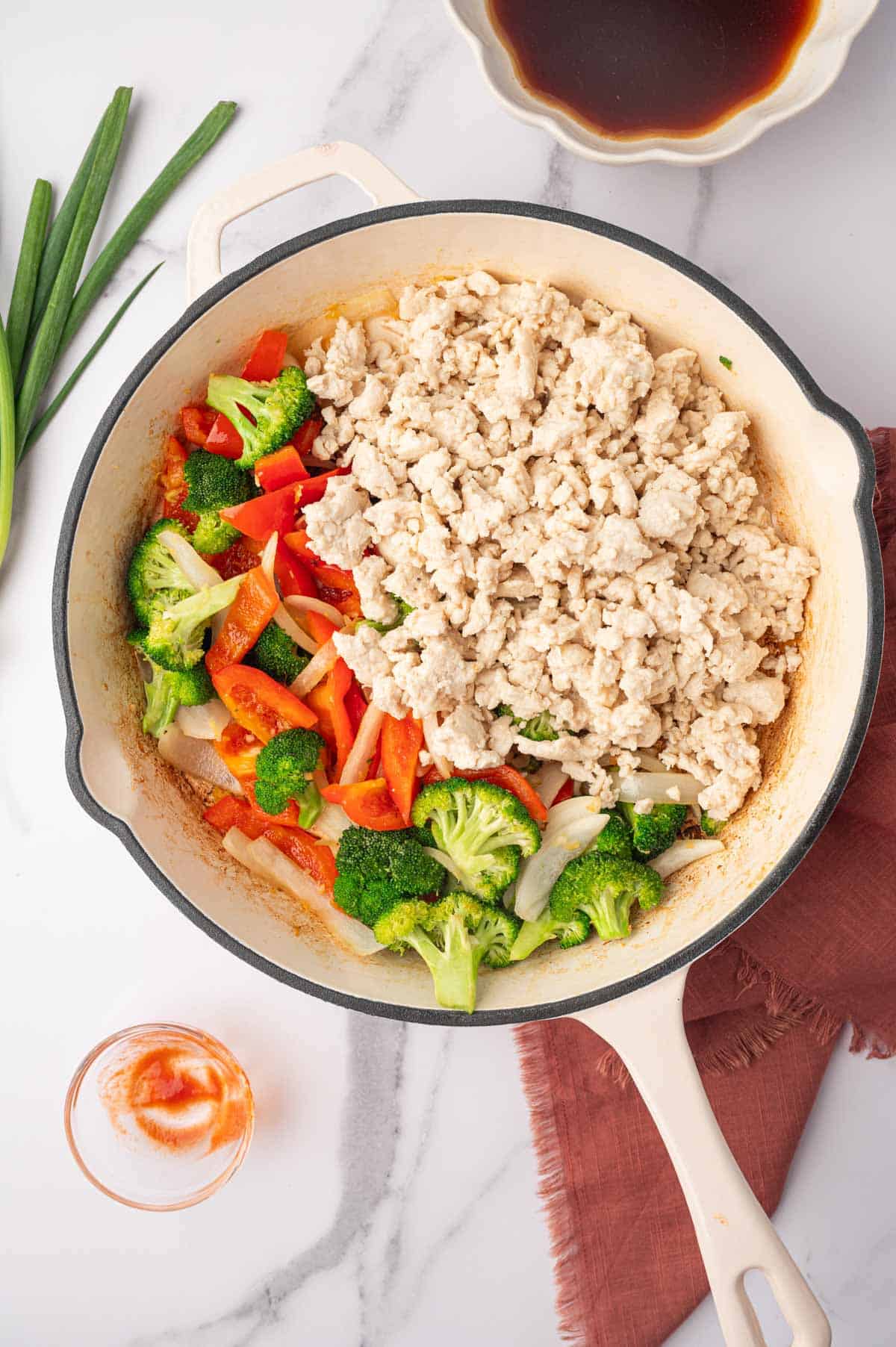 Cooked vegetables and ground chicken in a white skillet.