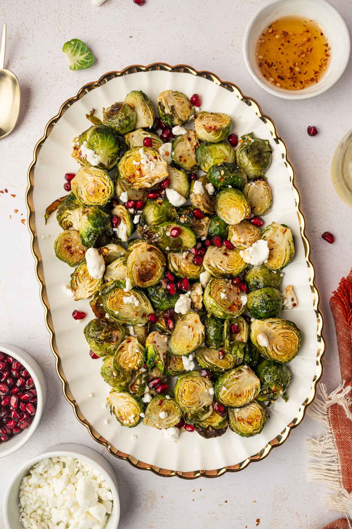 Hot honey Brussels sprouts garnished with pomegranate seeds and goat cheese placed in a white platter with gold rim