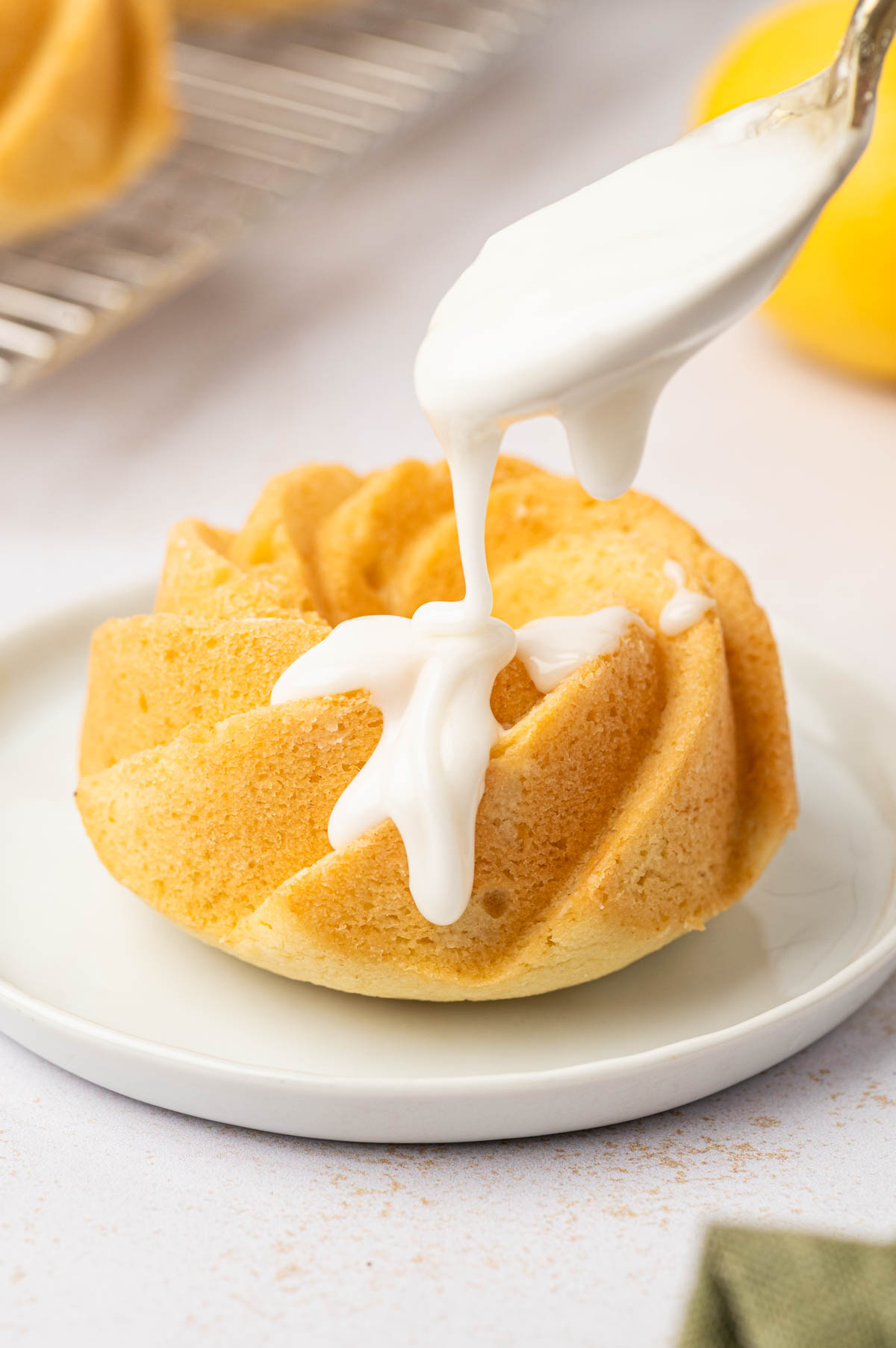 Lemon glaze drizzled over lemon mini bundt cake in a white plate.