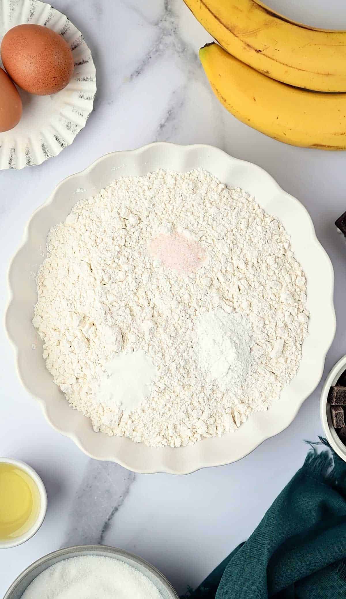 Dry ingredients added to a white bowl to make banana chocolate chunk muffins.