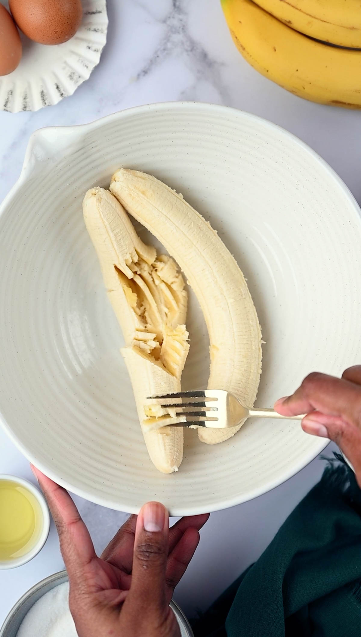 Banna being mashed with a fork in a large bowl for Banana Chocolate Chunks Muffins