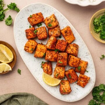 Blackened salmon bites in a oval platter arranged beautifully and garnished with parsley and lemon wedges in the side.