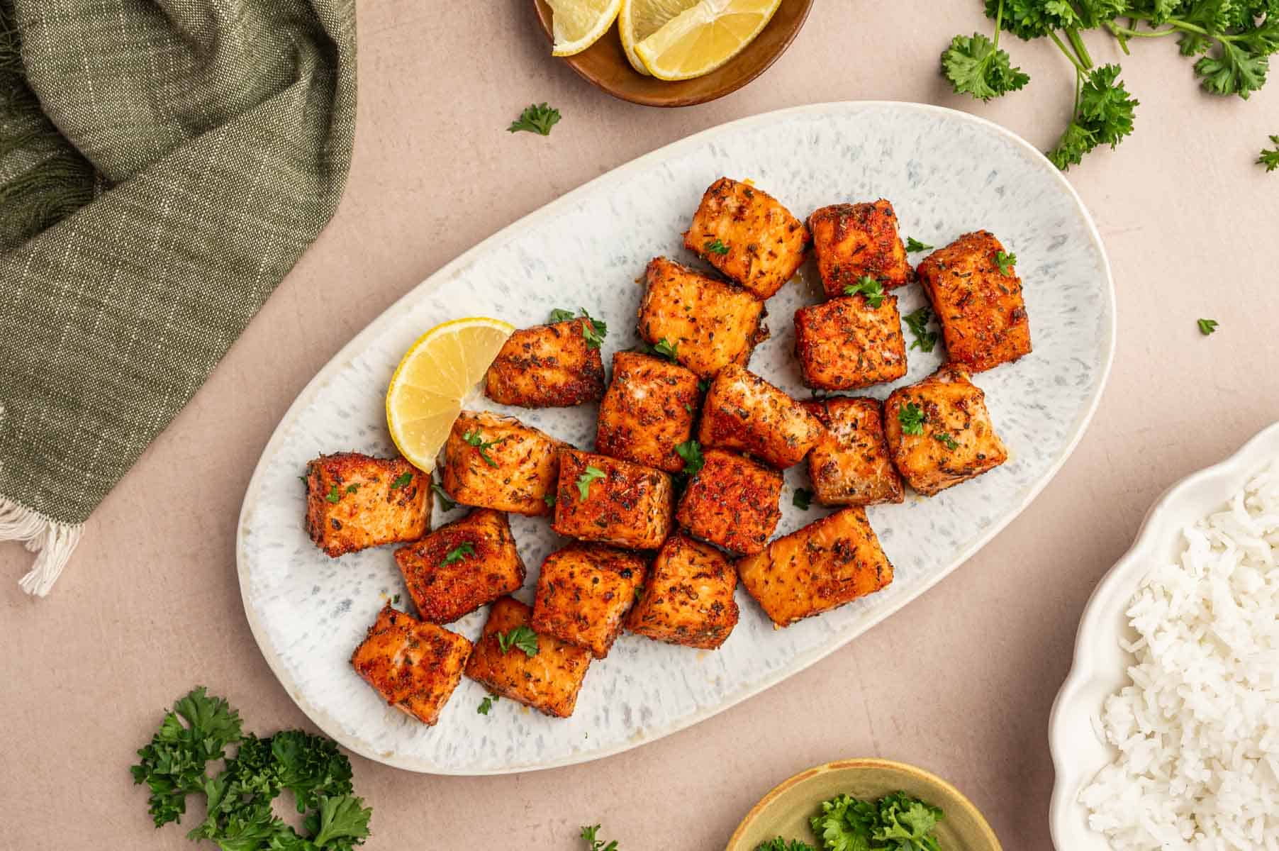 horizontal image of balckened salmon bites in a oval plate with garnishes on the sides.