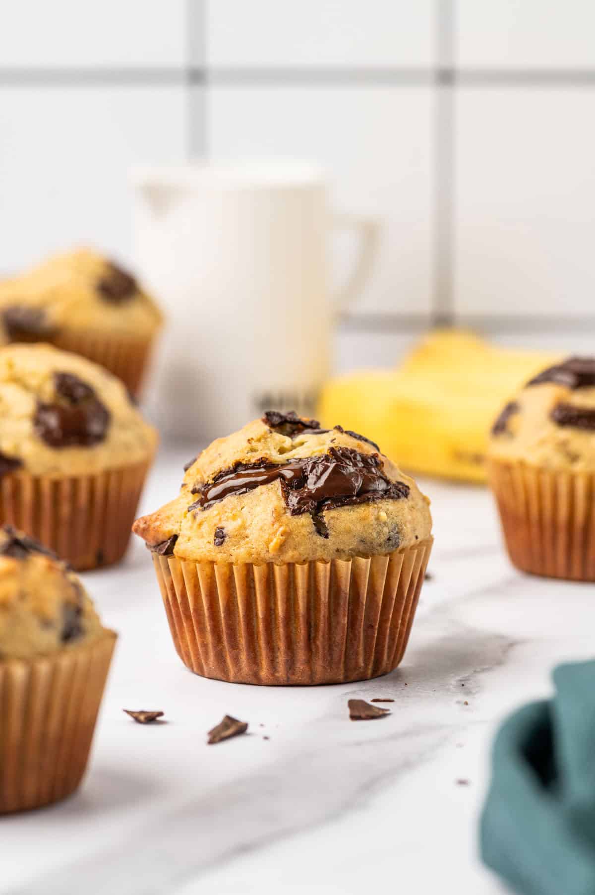 Banana chocolate chunk muffins in a marble surface, banana in the background.