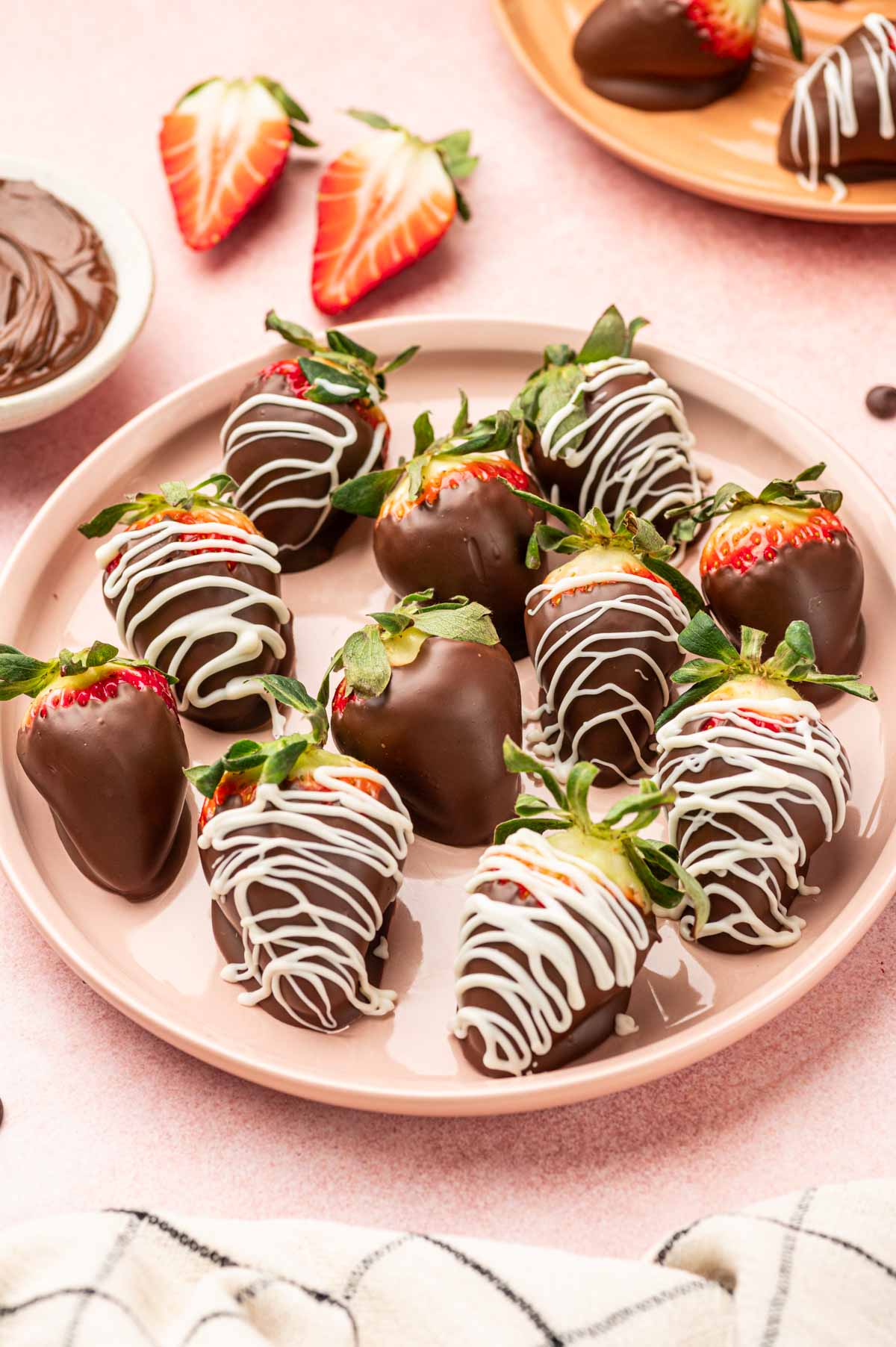 In a plate full of Nutella covered strawberries with pink background. Nutella is placed in a bowl in the side.