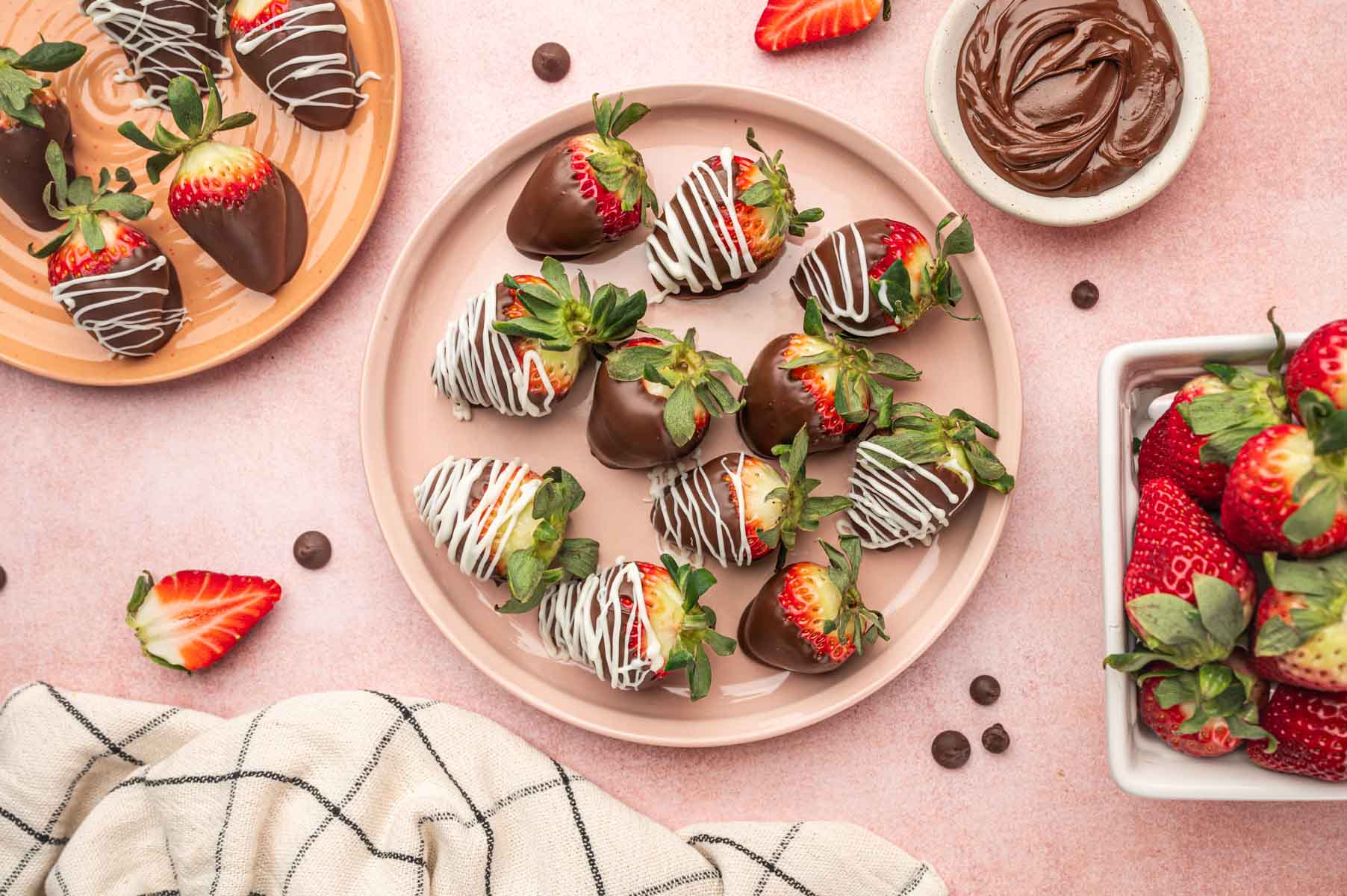 Nutella covered strawberries in a pink plate with nutella in the side along with fresh strawberries.