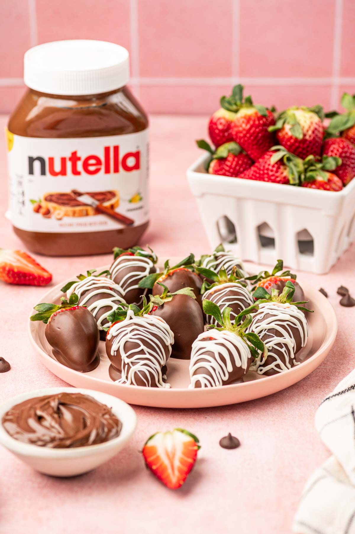 Nutella coveres strawberries in a pink plate and pink background , nutella product in the behind along with the fresh strawberries.