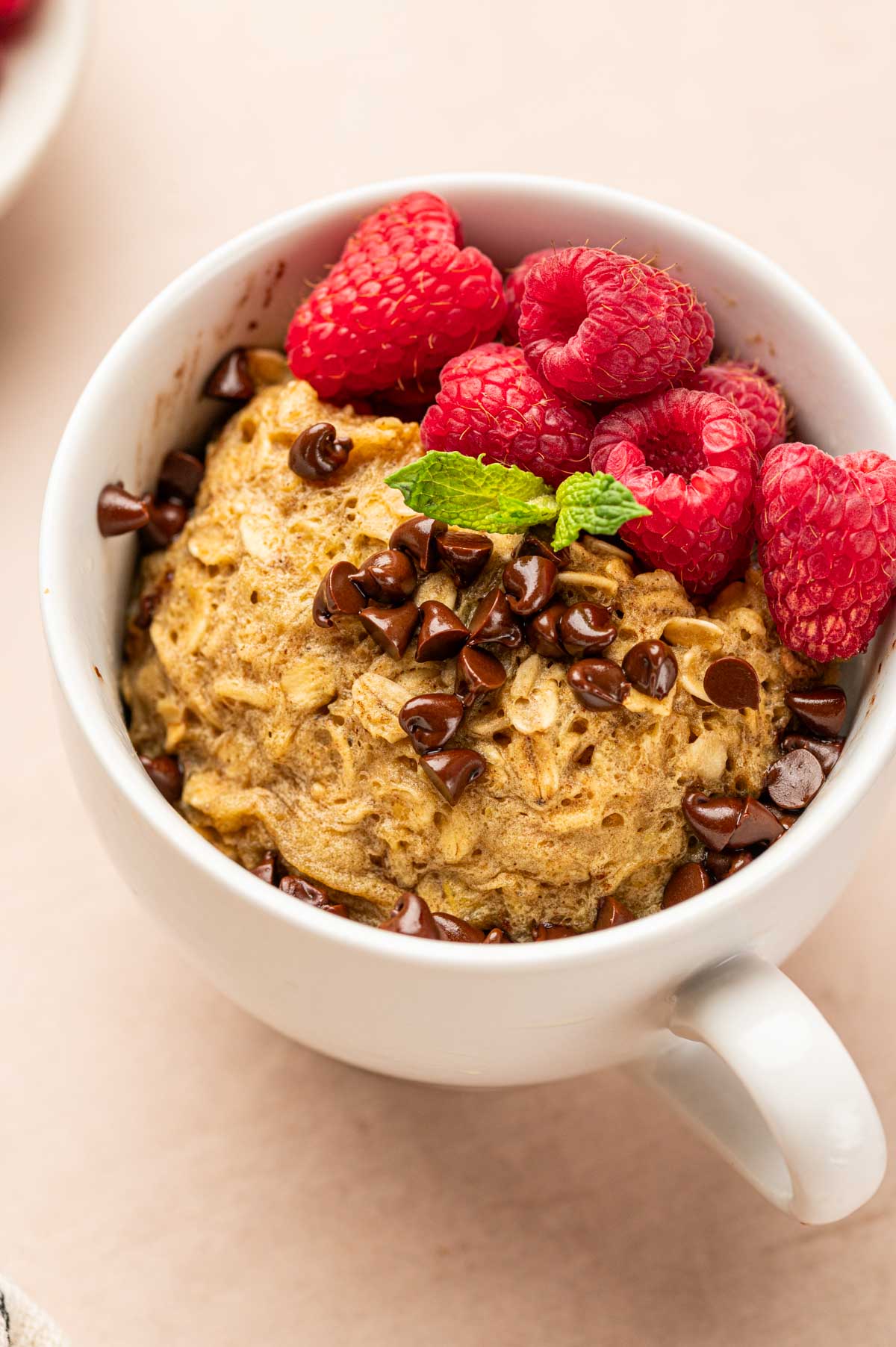 Healthy oatmeal mug cake toppedd with mini chocolate chips and fresh raspberries and fresh mint.