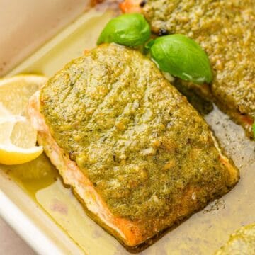 CLose up shot of pesto butter salmon garnished with basil and lemon wedges.