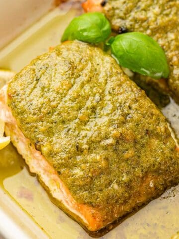 CLose up shot of pesto butter salmon garnished with basil and lemon wedges.