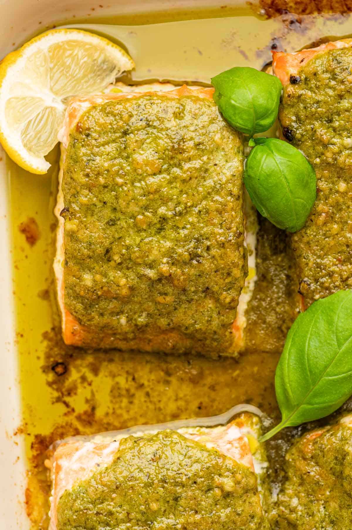 Baked  Pesto Salmon Butter in a baking dish close up shot ganrished with basil and lemon wedges.