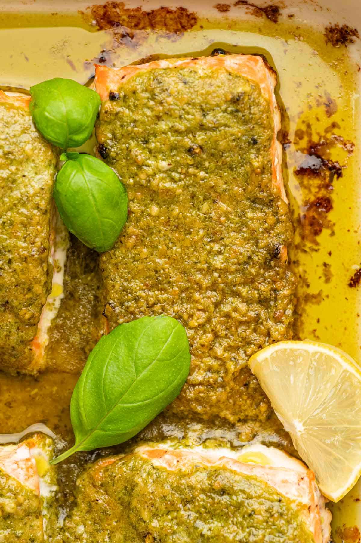 CLose up shot of pesto butter with salmon and garnished with lemon wedges in a baking dish.