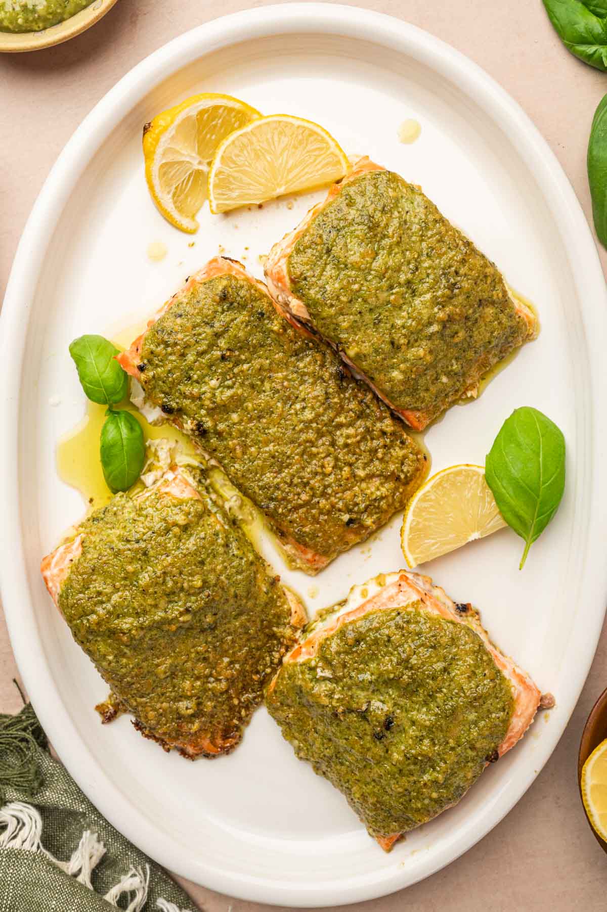 Pesto Butter Salmon served in a white oval platter garnished with basil and lemon wedges.