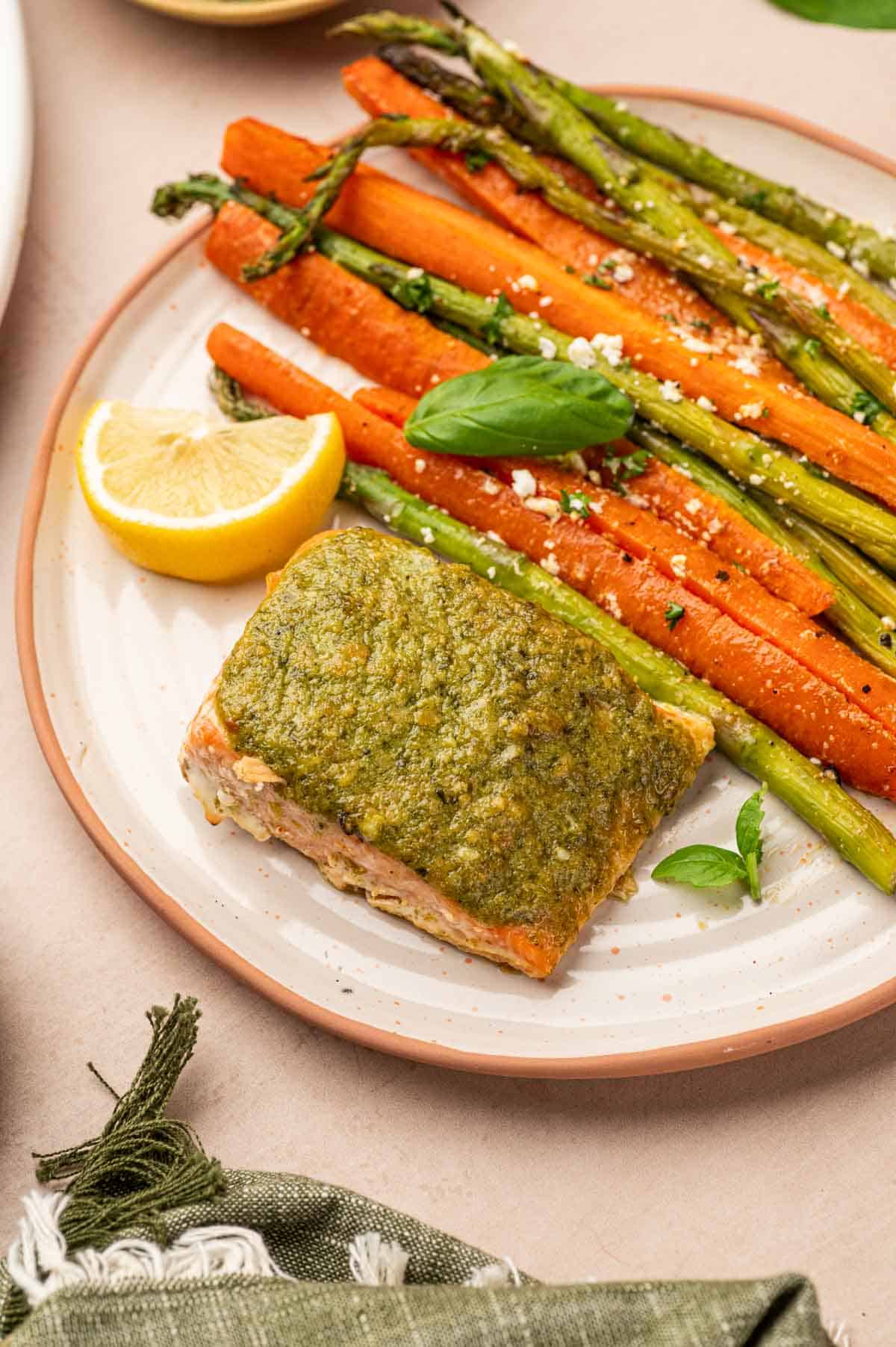 Salmon Pesto butter served in a plate with roasted carrots and asparagus in a orange plate.