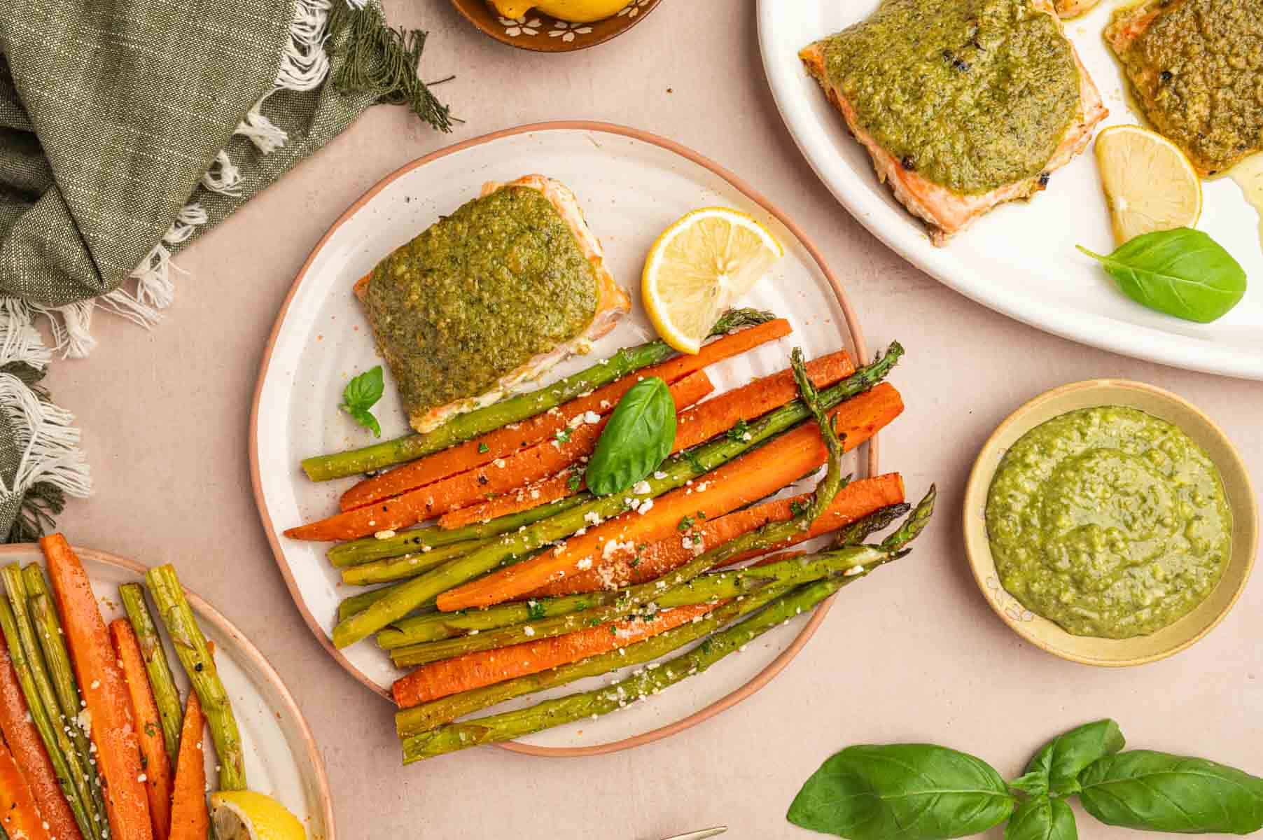 Horizontal shot of pesto butter salmon served with roasted veggies. Pesto sauce placed in a bowl aside.