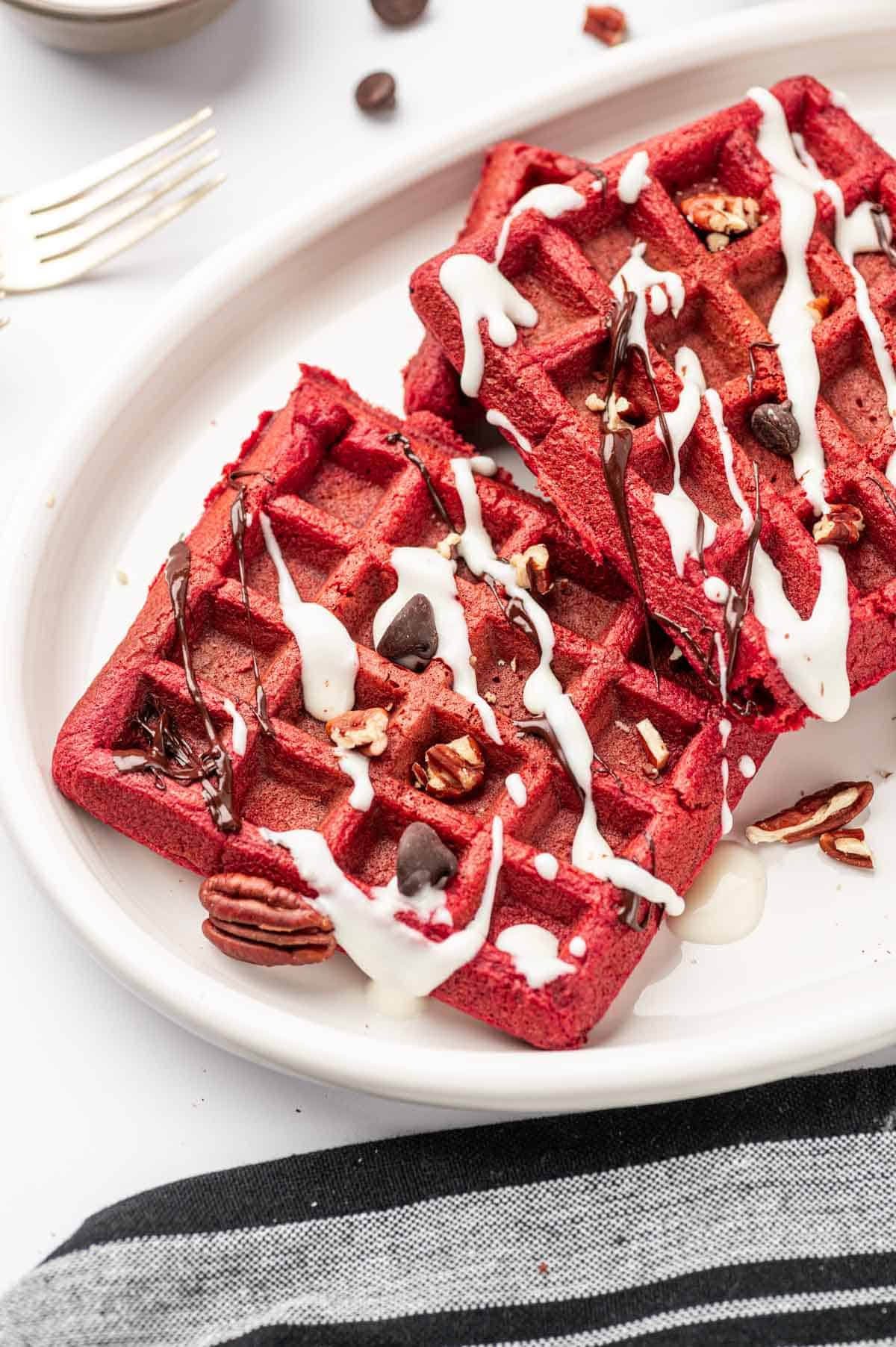 Backlit shot of red velvet cake mix waffles topped with pecans and chocolate chips with cream cheese drizzle and Chocolate ganache.