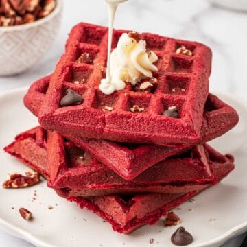 Stacked red velvet ake waffles , whipped cream topped with pecans and chocolate chips. Cream cheese drizzled over.