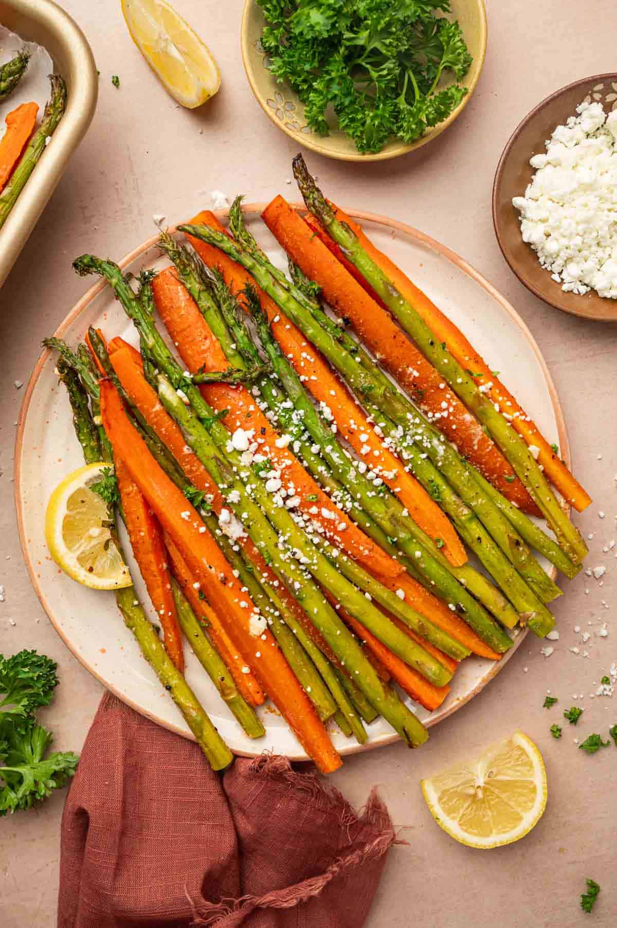 Roasted carrots and asparagus served ibuprofen a light orange plate and beautifully ganrished with goat cheese and parsley.