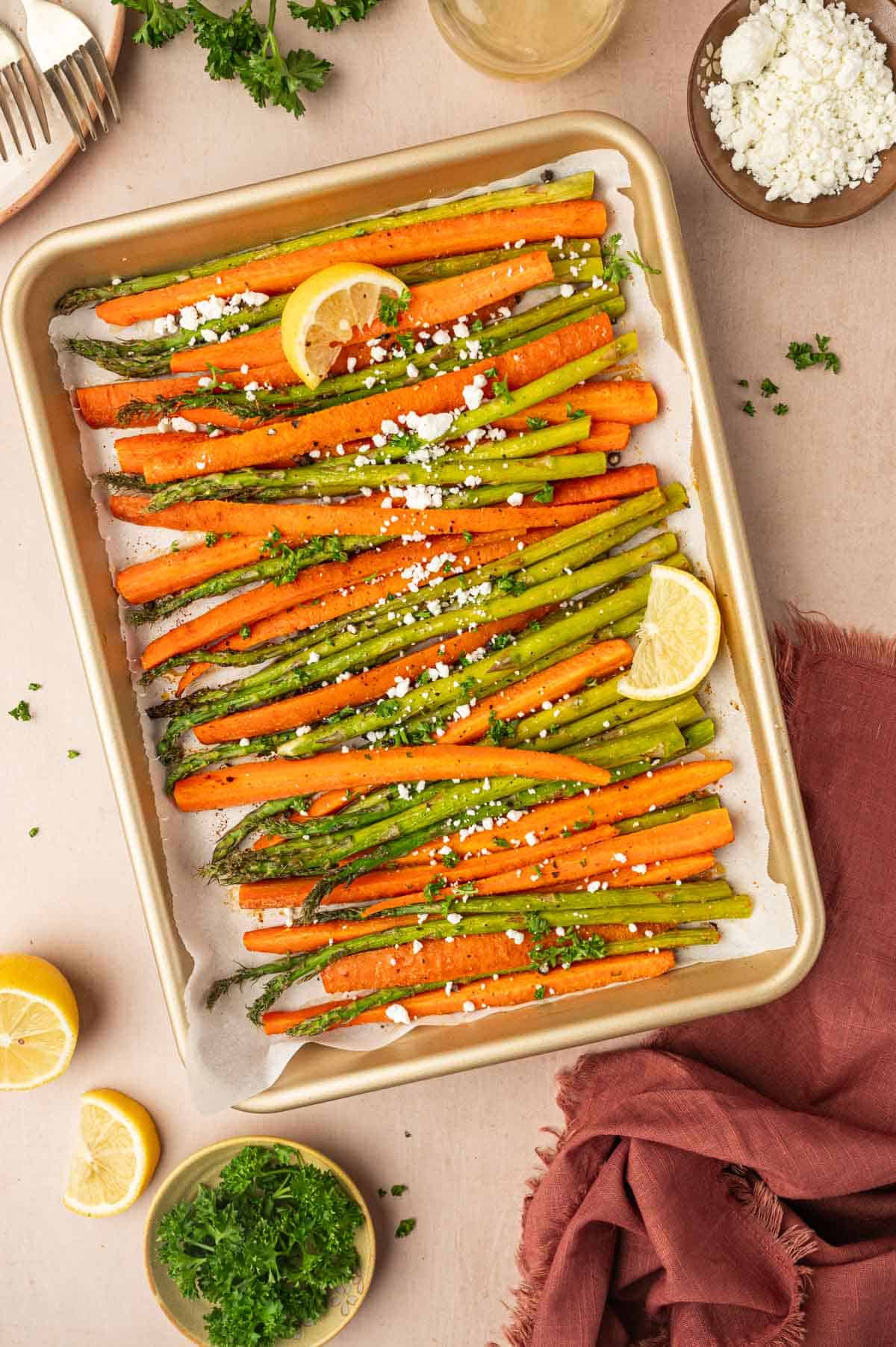 Roasted asparagus and carrots in a baking tray garnished with crumbled goat cheese and parsley.