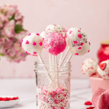 Homemade Valentine cake pops with cake mix arranged in a glass jar filled with sprinkles.