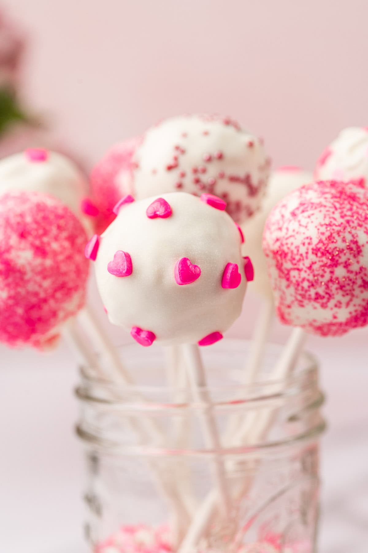 Beautifully decorated valentines day cake pops in a jar on a pink background.