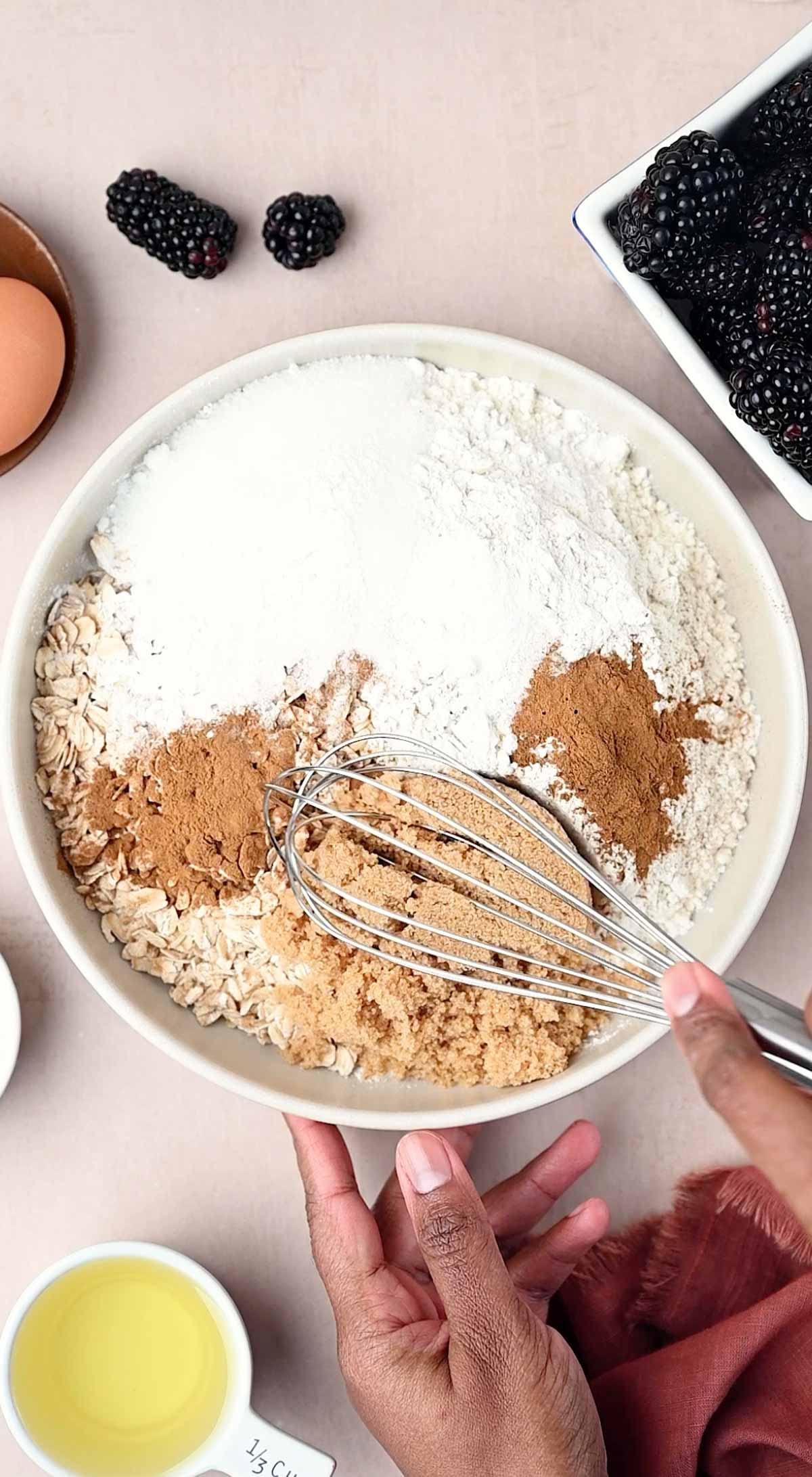 A hand is mixing the dry ingredients using a whisk for making the banana oatmeal muffins recipe.