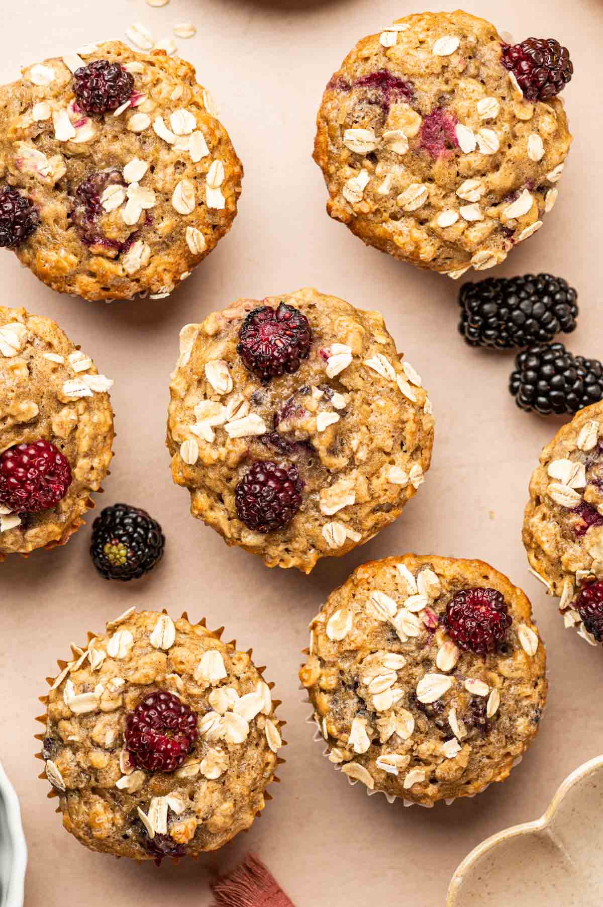 Flatlay image of banana blackberry oatmeal  muffins in a warm background with fresh blackberries around.