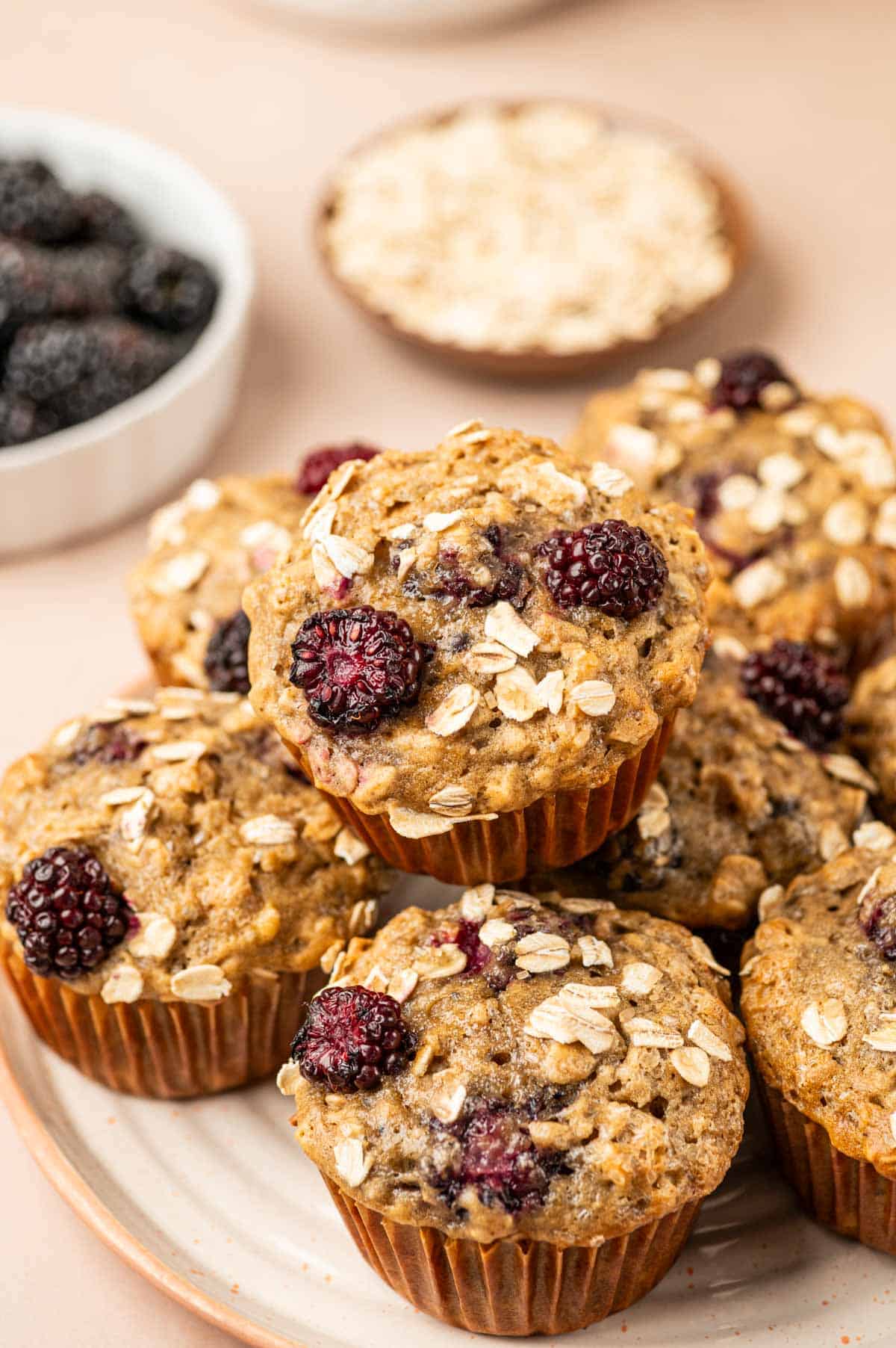 Banana blackberry oatmeal muffins placed in a plate on a warm background with fresh blackberries behind.