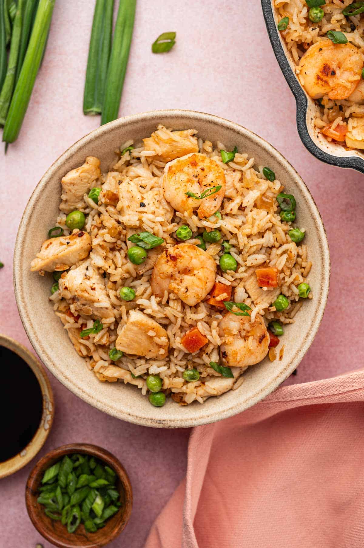 Chicken and shrimp fried rice served in a bowl, wooden bowl has green onions and another bowl has soy sauce.