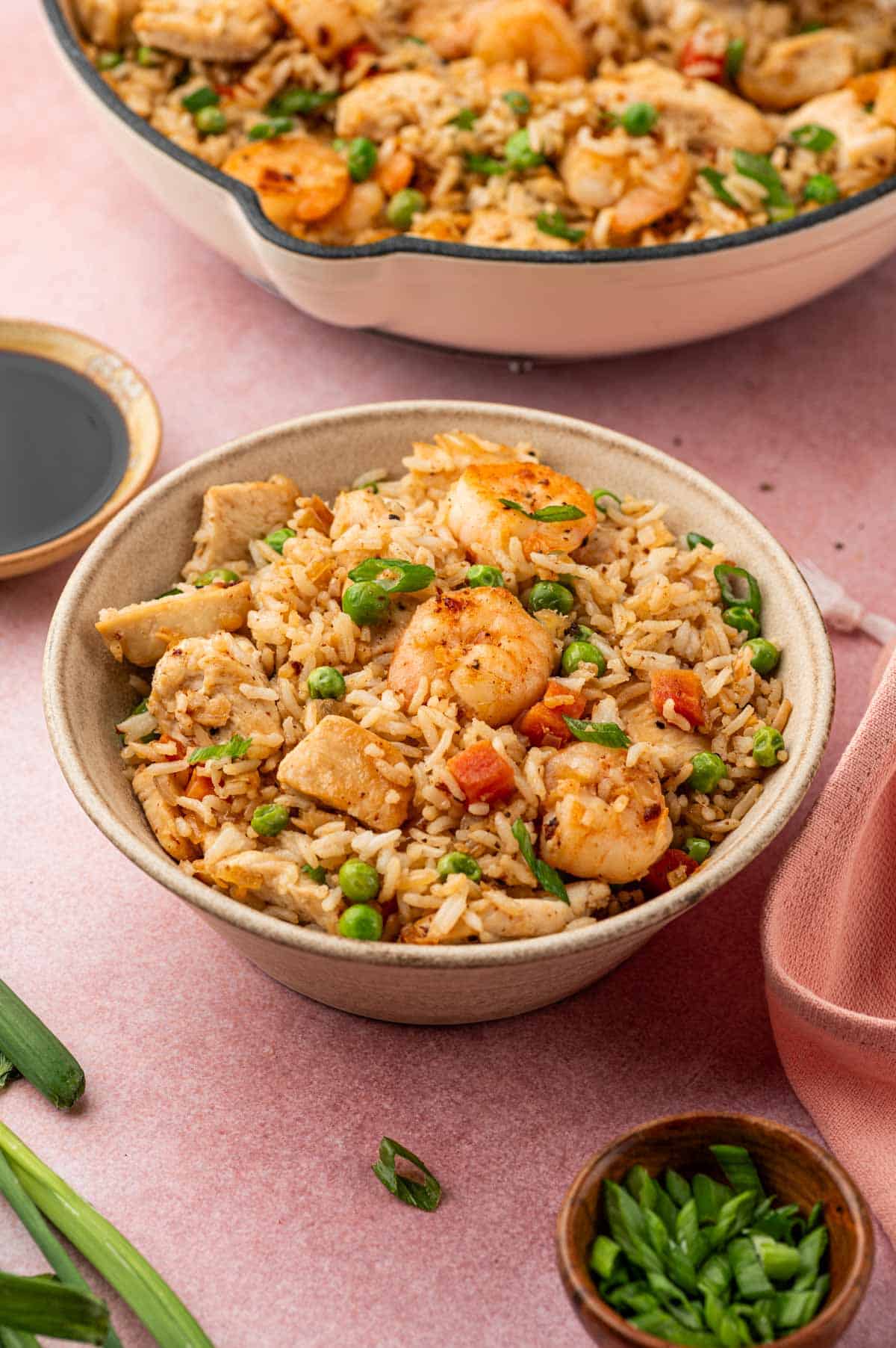 Chicken and shrimp fried rice in a bowl garnished with green onions in a warm background. Soy sauce placed in a dipping  plate.