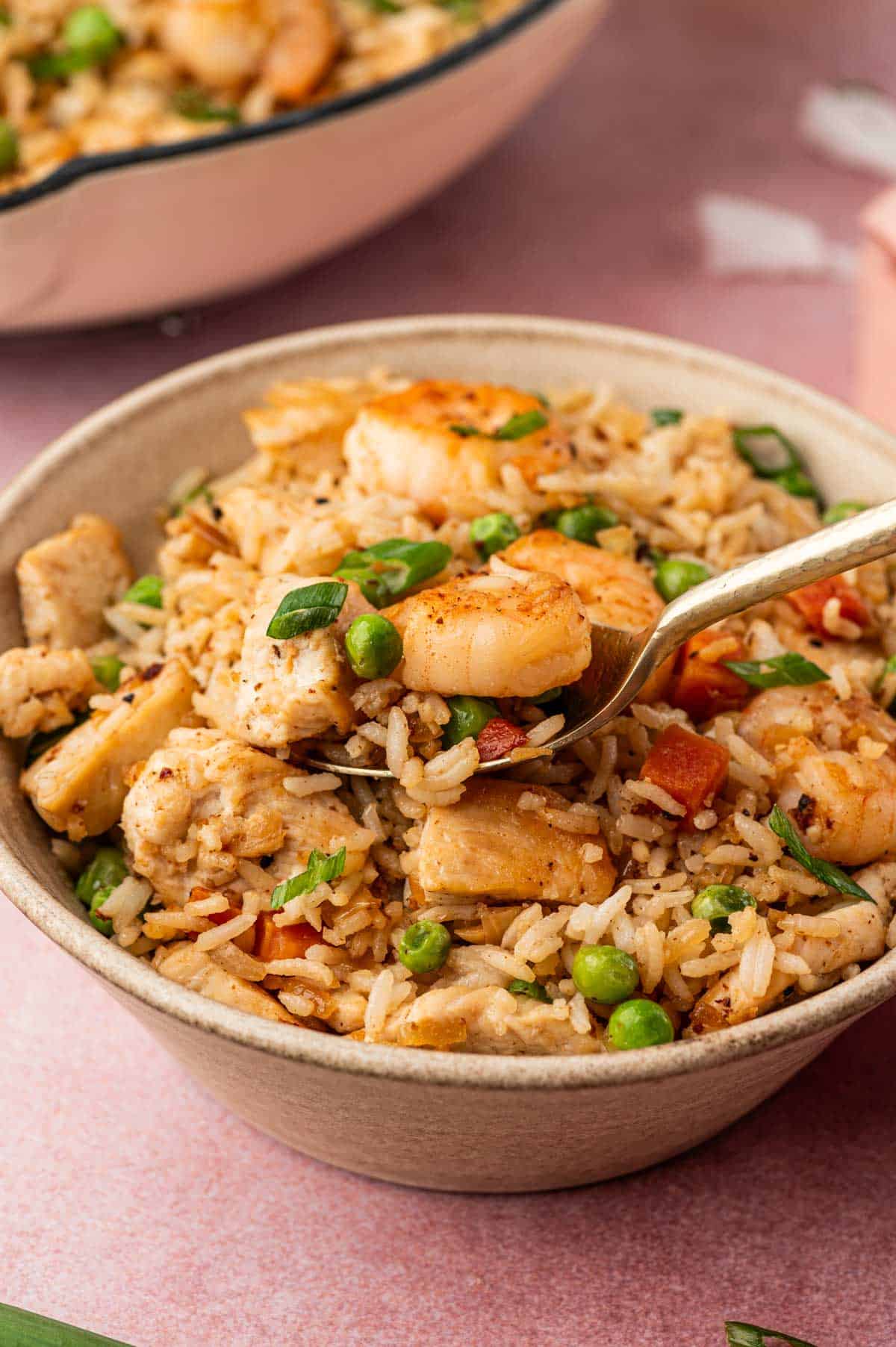 In a spoon Chicken and shrimp fried rice is being scooped from the serving bowl.