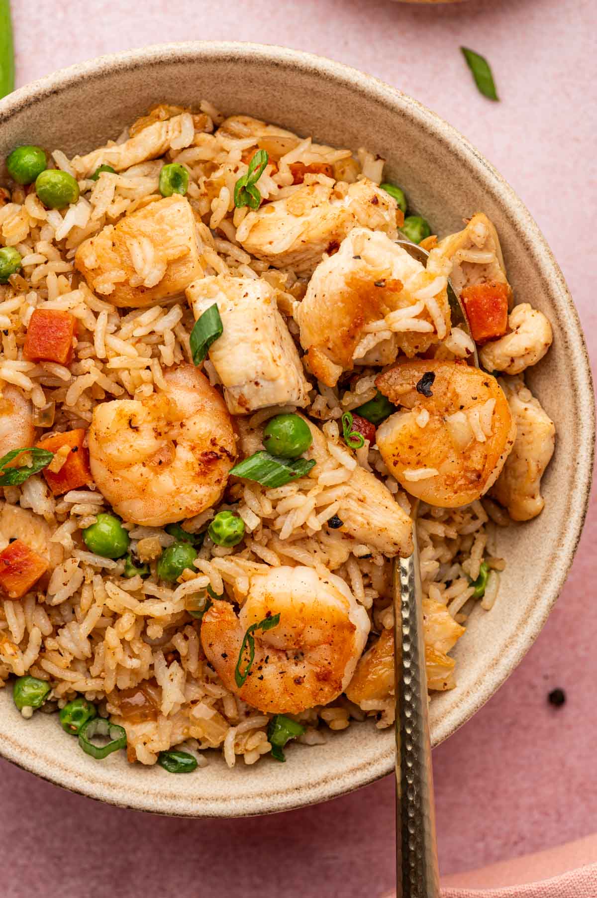 In a spoon full of Chicken and shrimp fried rice over a serving bowl.