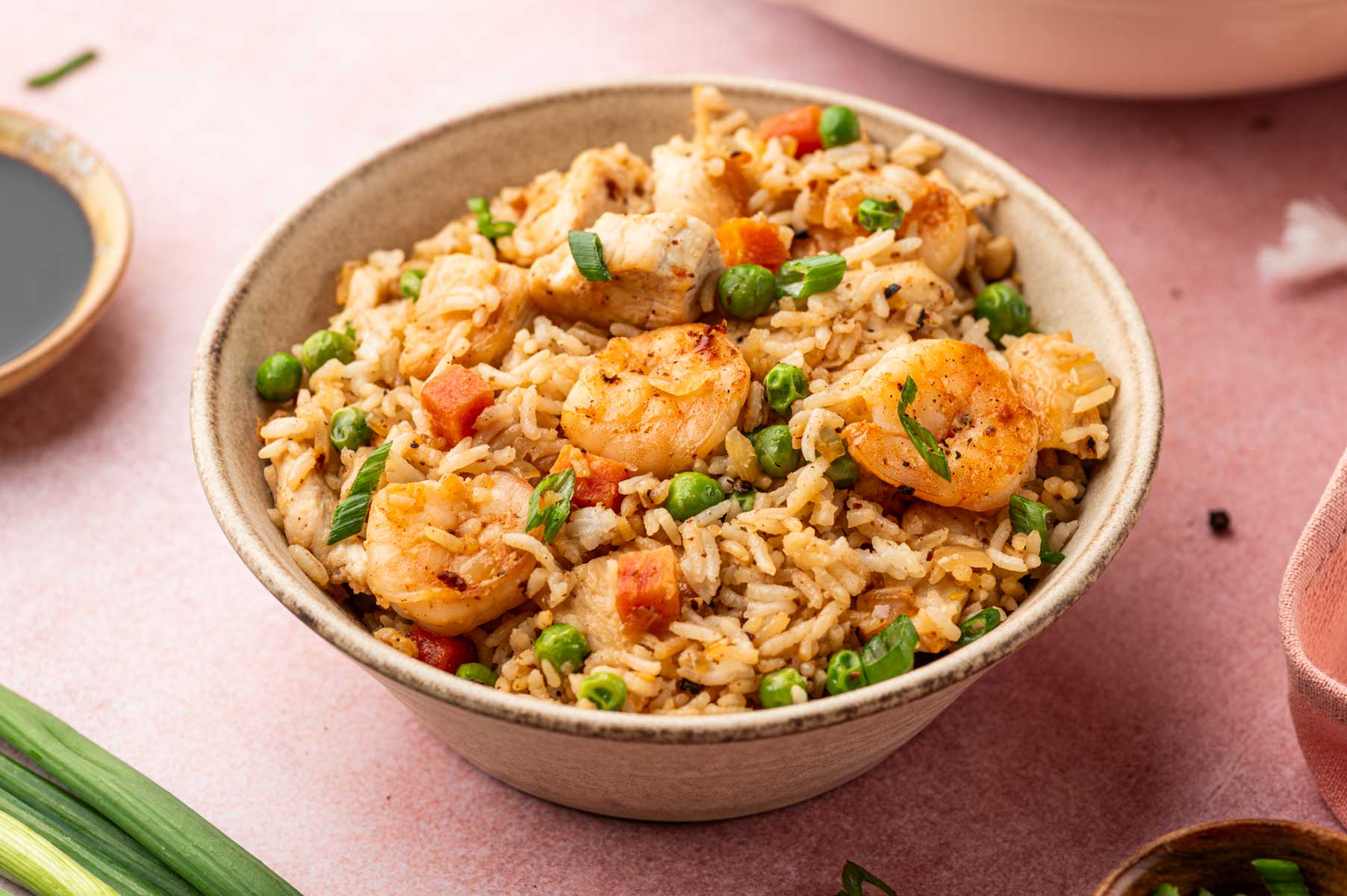 Horizontal image of Chicken and shrimp fried rice recipe served in a warm bowl in a pink background.