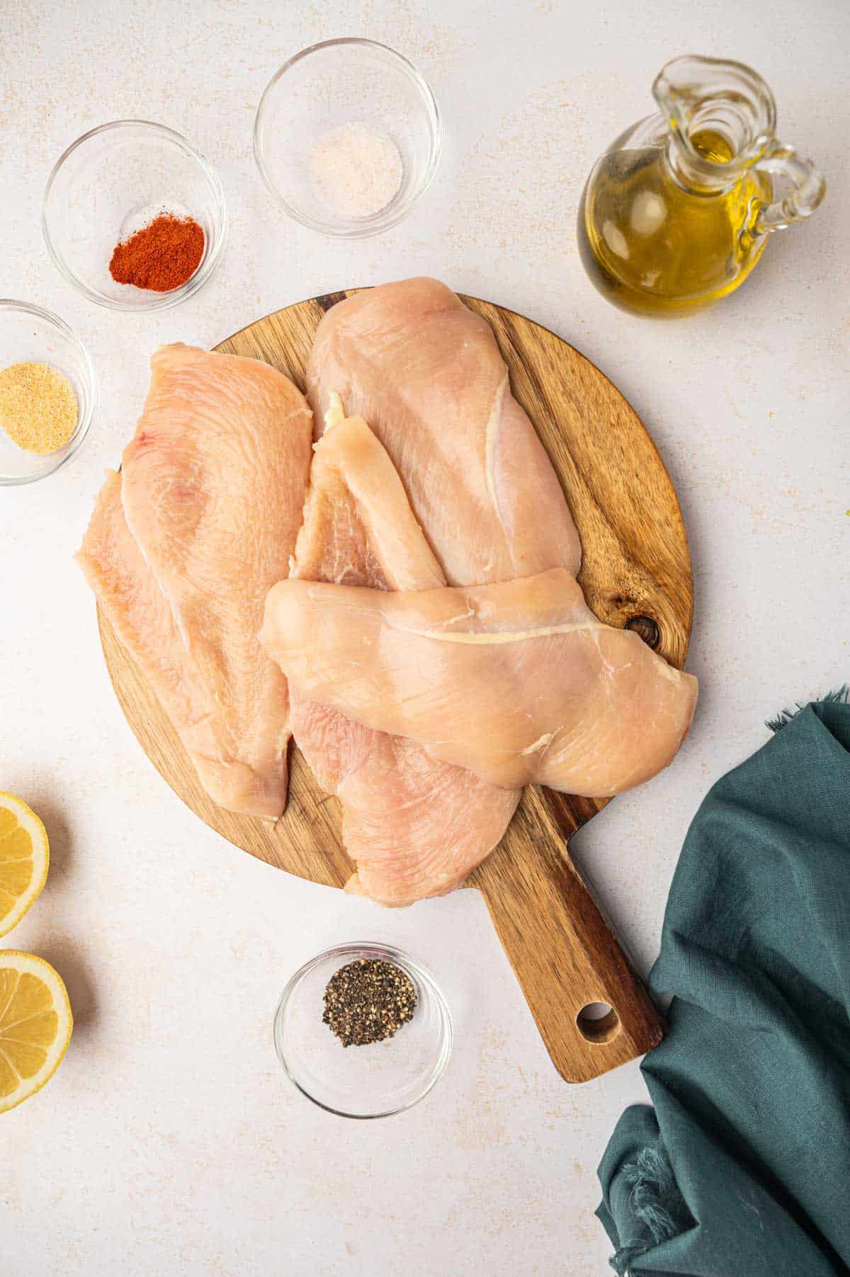 The Chicken breasts are sliced horizontally and placed in a wooden cutting board surrounded by the seasonings.