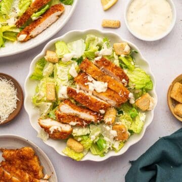 Crispy chicken caesar salad in a white bowl accompanied by a bowl homemade caesar salad dressing.